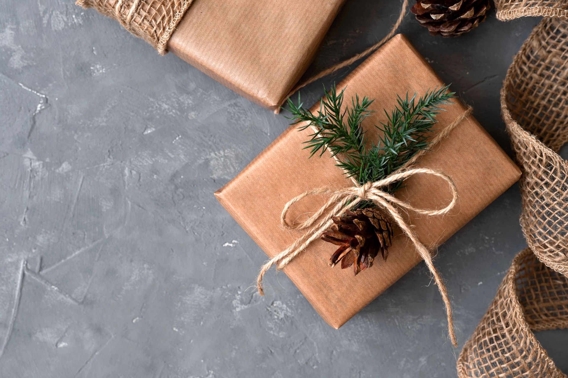 Aesthetic Christmas presents on gray table background. Brown gift boxes decorated with crafter paper, conifer twigs and pines. Sustainable ecological winter holiday celebration concept